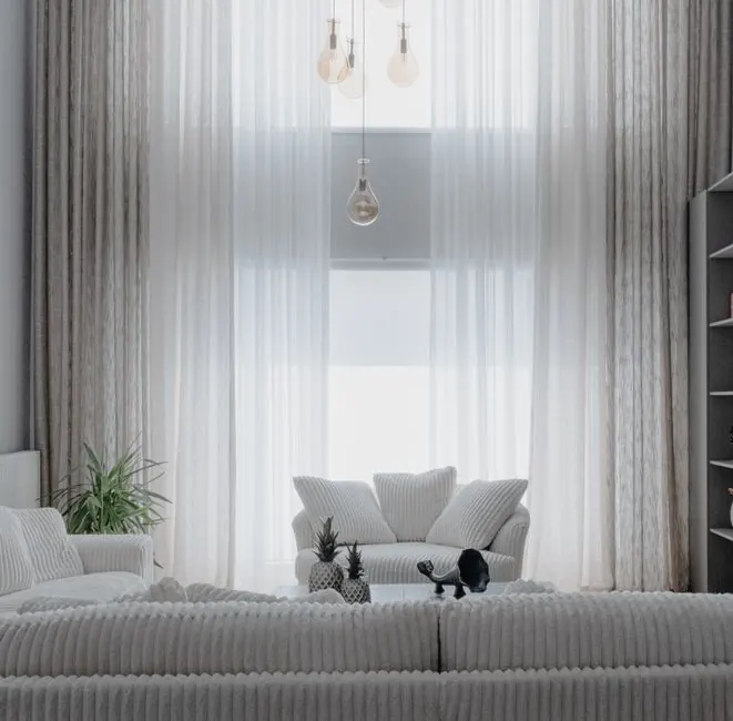 A minimalist living room with soft white sofas and large curtains, creating a cozy atmosphere.