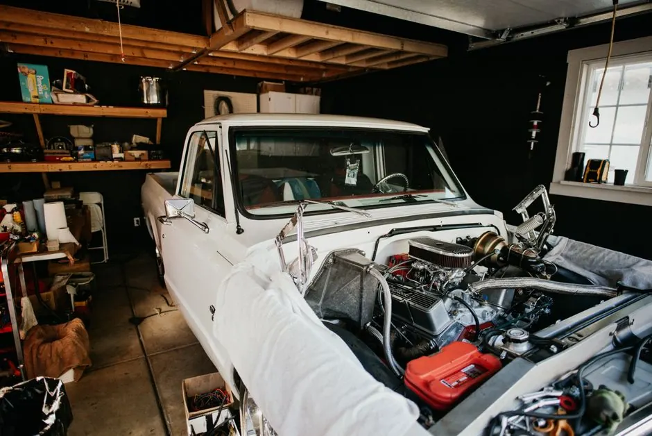A vintage pickup truck undergoing engine repairs in a well-equipped home garage.