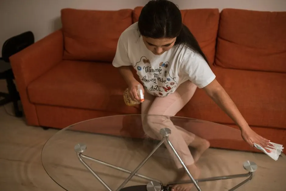 Adult woman wiping a glass table with spray in a cozy living room setting.