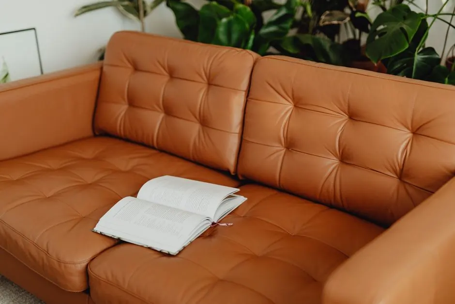 Elegant brown leather sofa with an open book, surrounded by vibrant houseplants, perfect for relaxation.